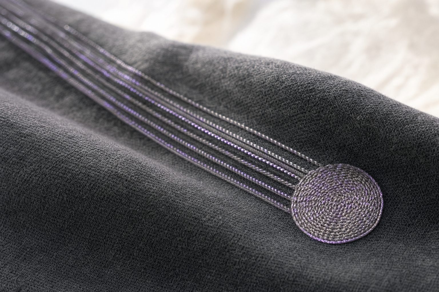 Close-up of an embroidered textile pressure sensor: conductive traces stitched into dark fabric leading to a circular sensing pad